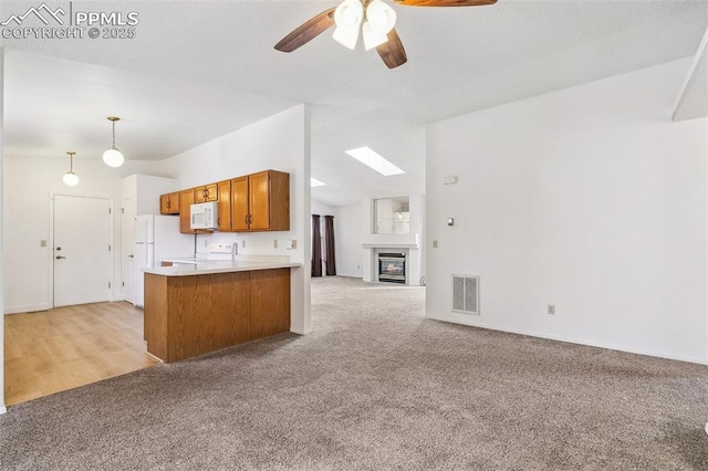 kitchen with vaulted ceiling, light carpet, kitchen peninsula, pendant lighting, and white appliances