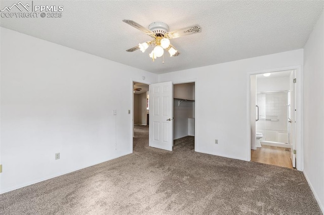 unfurnished bedroom with connected bathroom, a spacious closet, a textured ceiling, and carpet flooring