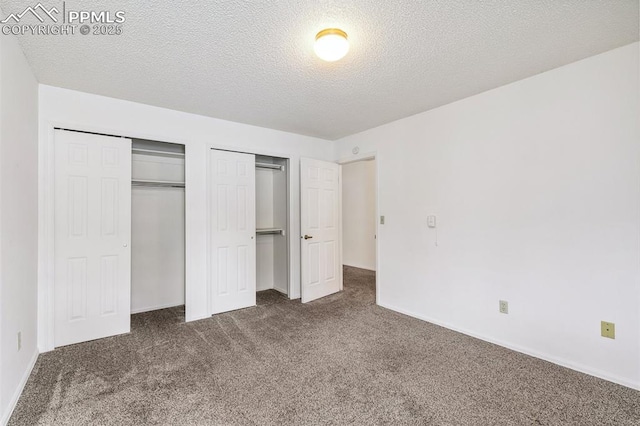 unfurnished bedroom with dark carpet, a textured ceiling, and two closets