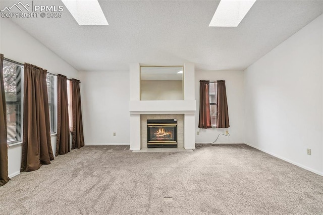 unfurnished living room featuring carpet flooring, a tiled fireplace, vaulted ceiling with skylight, and a textured ceiling