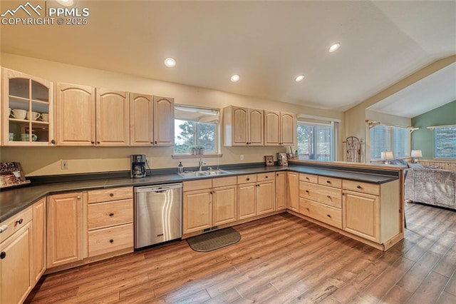 kitchen with dark countertops, lofted ceiling, glass insert cabinets, a sink, and dishwasher