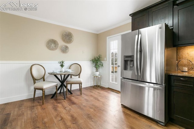 kitchen featuring ornamental molding, stainless steel fridge with ice dispenser, wood-type flooring, and light stone countertops