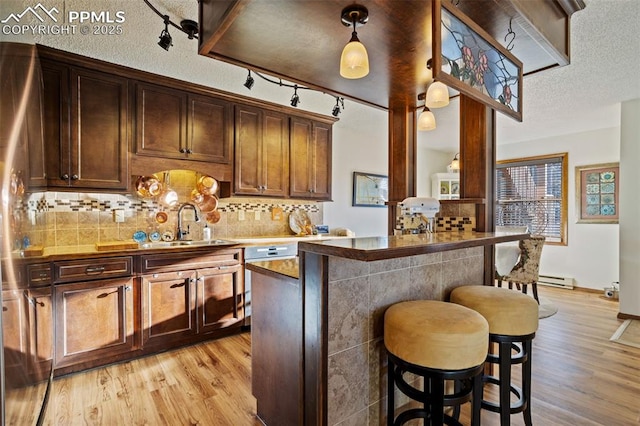 kitchen with sink, a kitchen breakfast bar, hanging light fixtures, and light hardwood / wood-style flooring