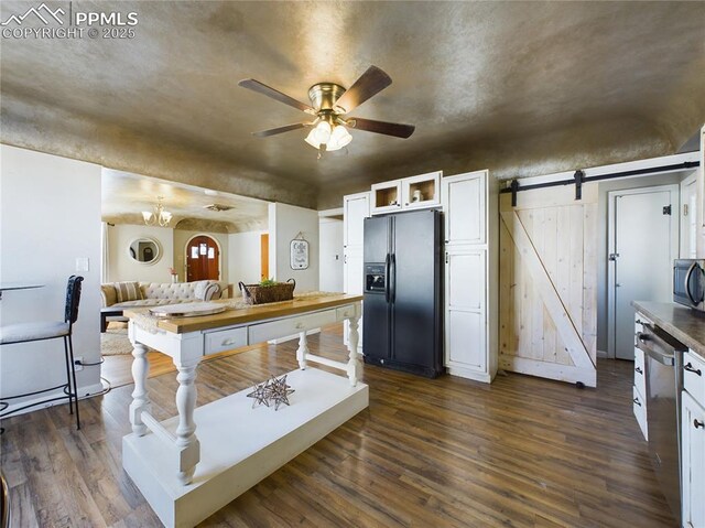 kitchen featuring stainless steel appliances, white cabinets, dark hardwood / wood-style flooring, ceiling fan with notable chandelier, and a barn door