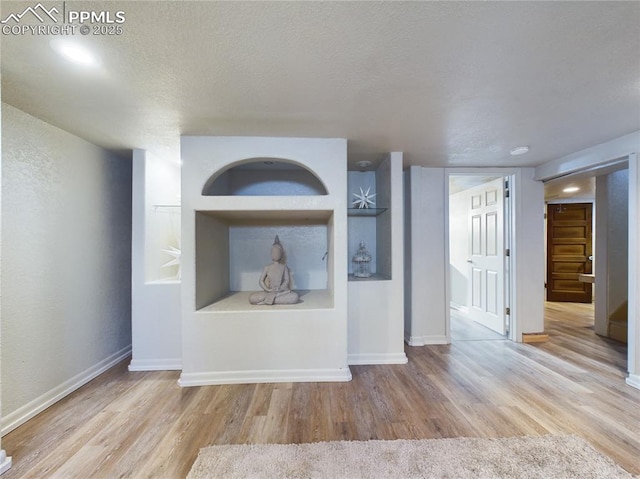 unfurnished living room featuring a textured ceiling, light hardwood / wood-style floors, and built in shelves