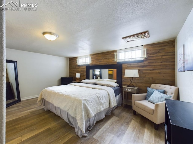 bedroom featuring hardwood / wood-style flooring, a textured ceiling, and wood walls