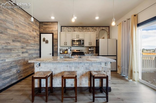 kitchen featuring hanging light fixtures, appliances with stainless steel finishes, a breakfast bar area, and light stone counters