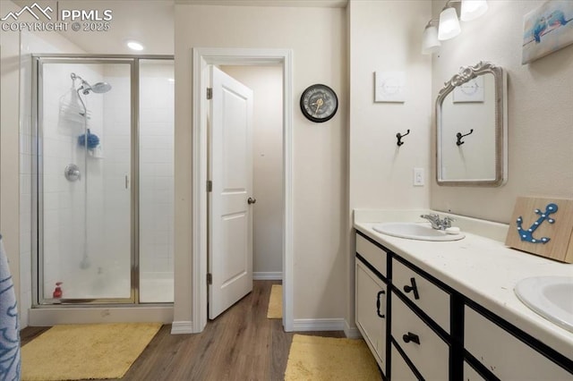 bathroom featuring double vanity, baseboards, wood finished floors, a shower stall, and a sink