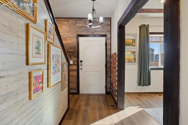 foyer entrance with wooden walls, a chandelier, and wood finished floors