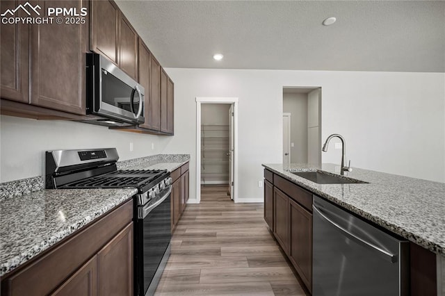 kitchen featuring sink, light hardwood / wood-style flooring, appliances with stainless steel finishes, dark brown cabinets, and light stone counters