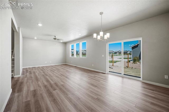 interior space featuring ceiling fan with notable chandelier, a wealth of natural light, light hardwood / wood-style floors, and a textured ceiling