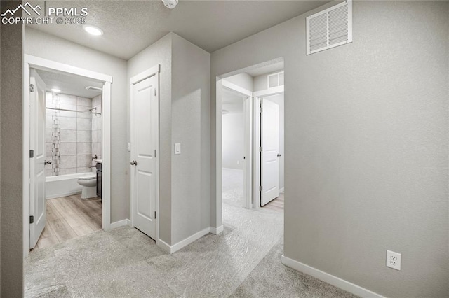 corridor with light carpet and a textured ceiling