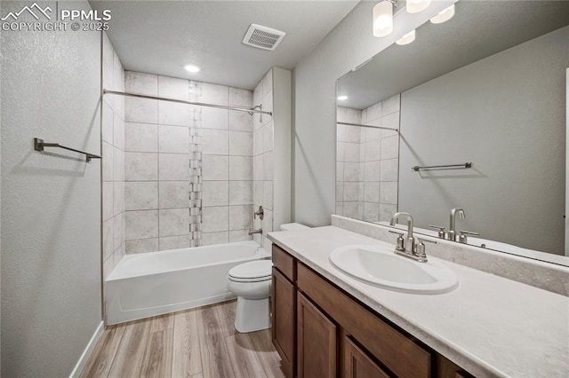 full bathroom with hardwood / wood-style flooring, vanity, tiled shower / bath combo, and toilet