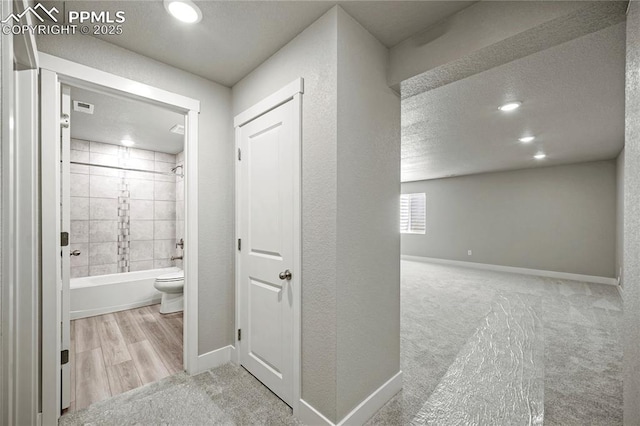 bathroom featuring a textured ceiling, wood-type flooring, toilet, and tiled shower / bath