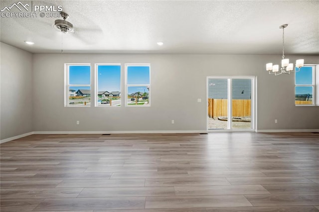 unfurnished room featuring ceiling fan with notable chandelier, wood-type flooring, and a textured ceiling