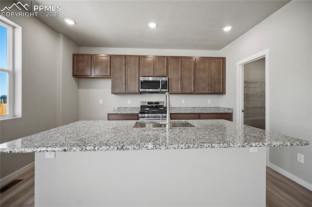 kitchen featuring light stone counters, stainless steel appliances, dark hardwood / wood-style flooring, and an island with sink