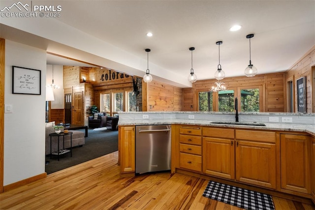 kitchen with wood walls, decorative light fixtures, dishwasher, sink, and light stone countertops