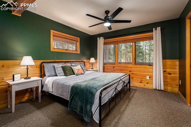 bedroom with ceiling fan, wood walls, and dark colored carpet