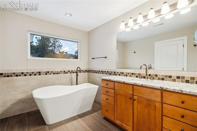 bathroom with vanity, a tub to relax in, and tile walls