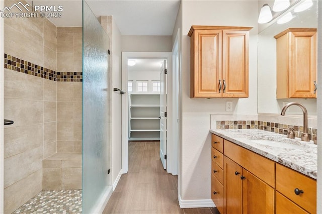 bathroom featuring tasteful backsplash, tiled shower, vanity, and wood-type flooring