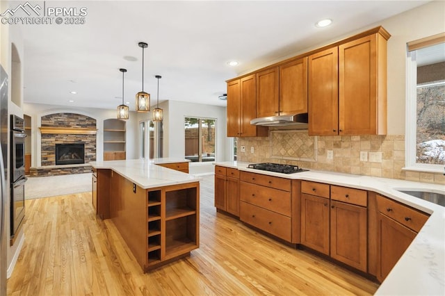 kitchen with black gas stovetop, a stone fireplace, light wood-type flooring, and decorative light fixtures