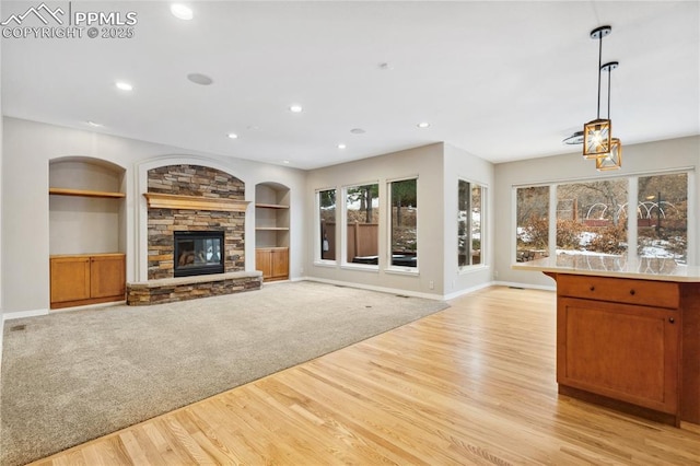 unfurnished living room featuring a stone fireplace, built in features, and light wood-type flooring