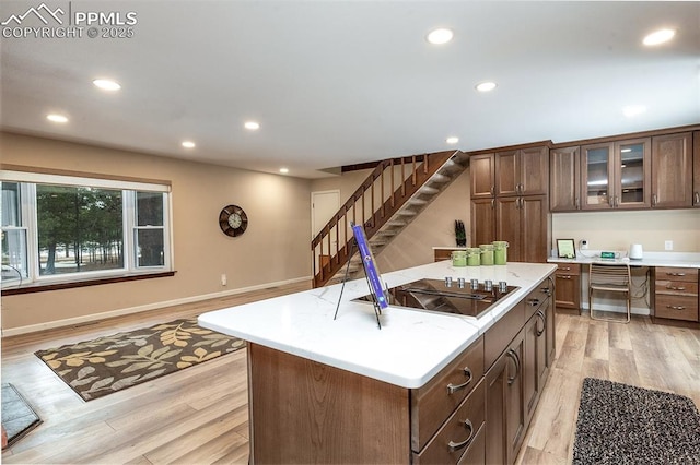 kitchen featuring black electric stovetop, light hardwood / wood-style floors, an island with sink, and built in desk