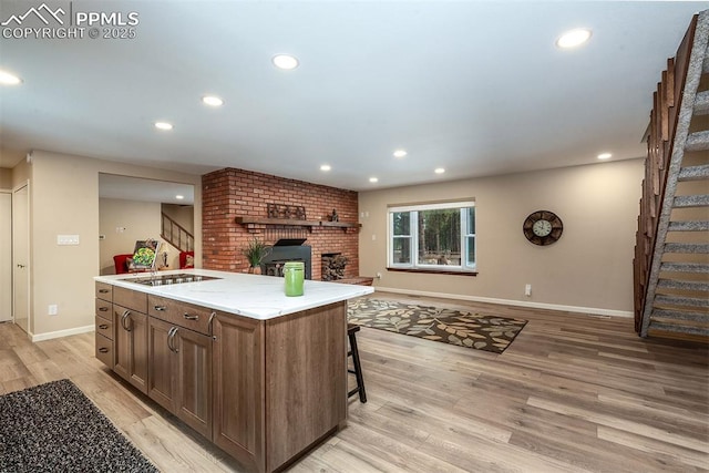 kitchen with a kitchen breakfast bar, a center island with sink, a fireplace, and light wood-type flooring