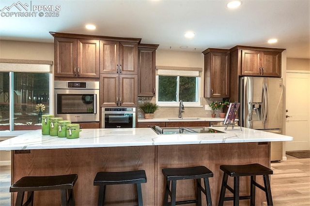 kitchen with sink, light hardwood / wood-style flooring, stainless steel appliances, a kitchen breakfast bar, and decorative backsplash