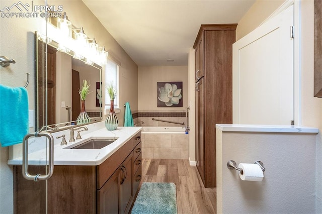 bathroom featuring hardwood / wood-style flooring, vanity, and tiled bath