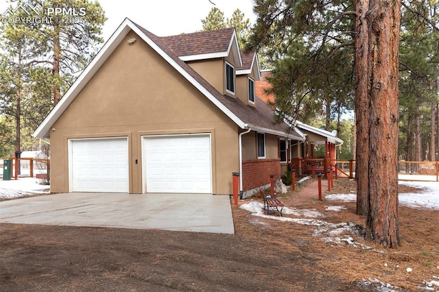 view of snow covered exterior with a shingled roof, driveway, a garage, and stucco siding