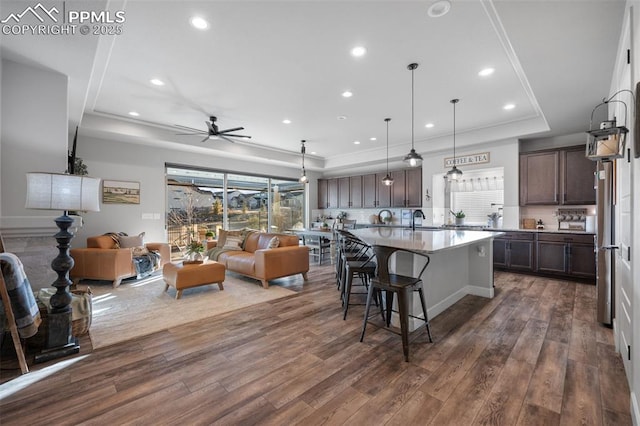 kitchen featuring a breakfast bar area, dark brown cabinets, a raised ceiling, pendant lighting, and a kitchen island with sink