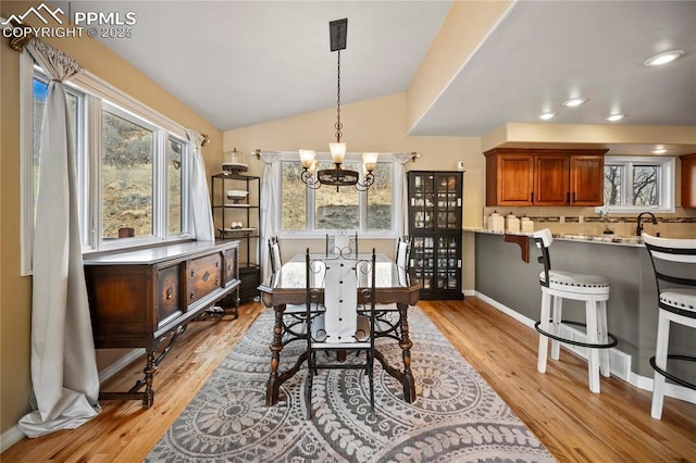 dining room featuring an inviting chandelier, sink, vaulted ceiling, and light wood-type flooring