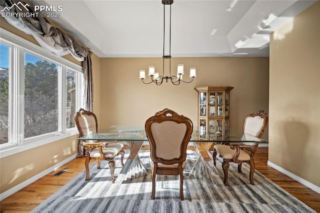 dining area featuring hardwood / wood-style flooring, a raised ceiling, and a chandelier