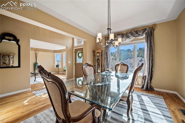 dining room featuring a raised ceiling, an inviting chandelier, and light wood-type flooring