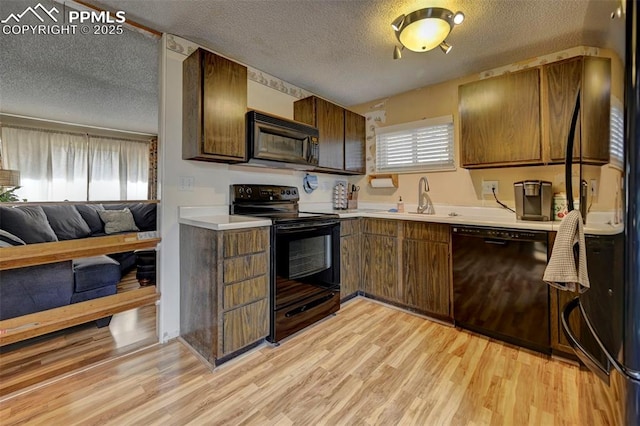 kitchen featuring sink, light hardwood / wood-style flooring, a textured ceiling, and black appliances