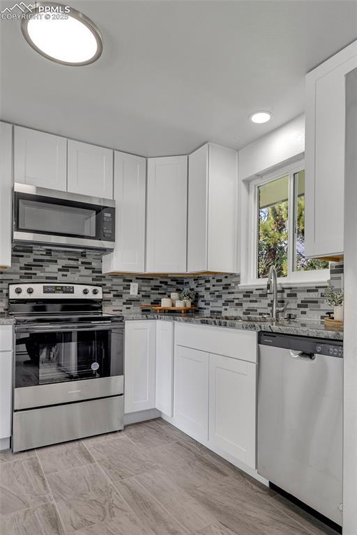 kitchen with appliances with stainless steel finishes, stone countertops, and white cabinets