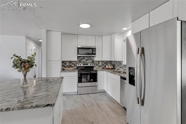 kitchen featuring tasteful backsplash, white cabinetry, sink, light stone counters, and stainless steel appliances