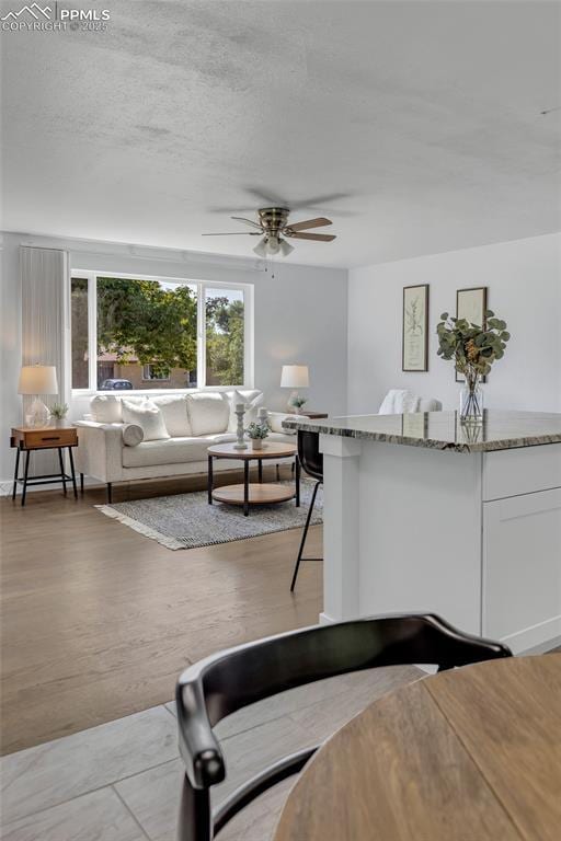 living room with ceiling fan, a textured ceiling, and light hardwood / wood-style floors