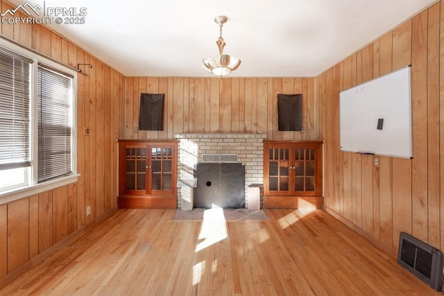 unfurnished living room with a brick fireplace, wood walls, and light hardwood / wood-style flooring