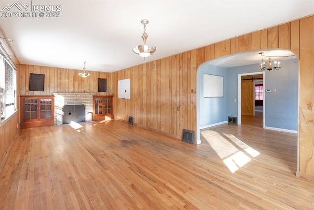 unfurnished living room featuring a barn door, light wood-type flooring, wooden walls, and a fireplace