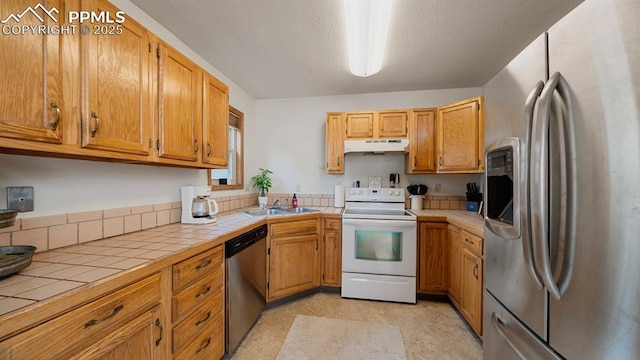 kitchen featuring appliances with stainless steel finishes, sink, tile counters, and a textured ceiling