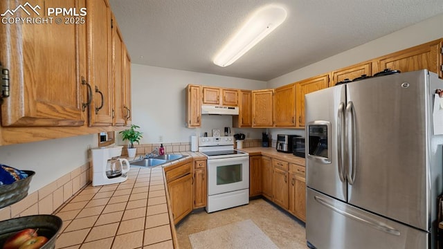 kitchen with electric stove, sink, a textured ceiling, stainless steel fridge with ice dispenser, and tile countertops