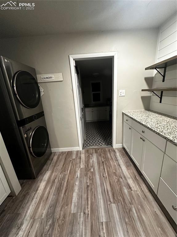 laundry room featuring cabinets, stacked washer / drying machine, and light hardwood / wood-style flooring