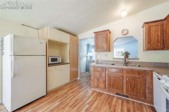 kitchen with vaulted ceiling, white appliances, sink, and light hardwood / wood-style flooring