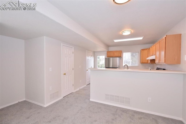 kitchen with light carpet, stainless steel fridge, light brown cabinetry, and kitchen peninsula