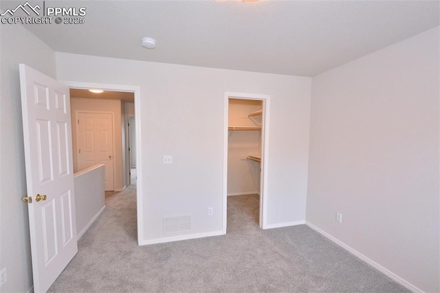 unfurnished bedroom with a spacious closet, light colored carpet, and a closet