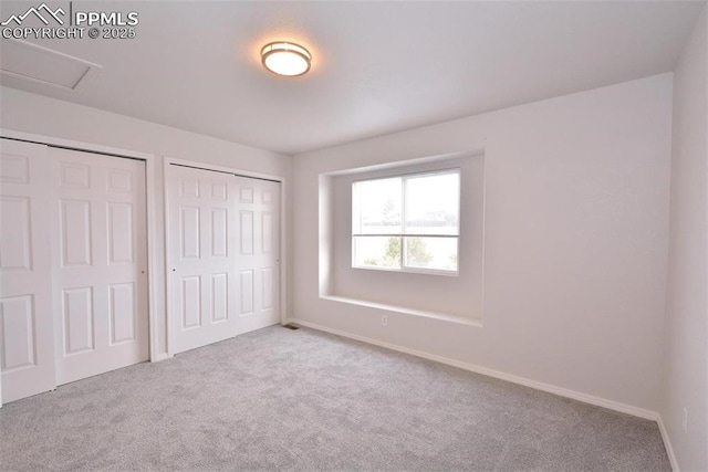 unfurnished bedroom with two closets and light colored carpet