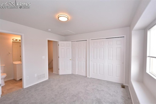 unfurnished bedroom with light carpet, connected bathroom, and two closets