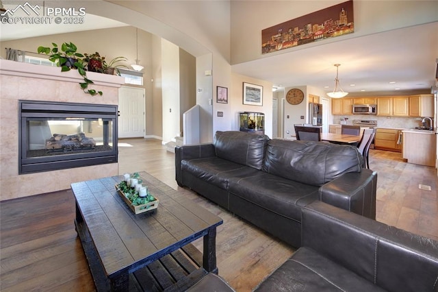 living room featuring high vaulted ceiling, sink, a tiled fireplace, and light hardwood / wood-style floors